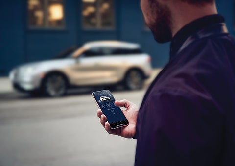A person is shown interacting with a smartphone to connect to a Lincoln vehicle across the street. | Bill Collins Lincoln of Louisville in Louisville KY