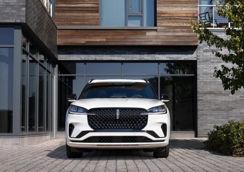 A white 2025 Lincoln Aviator® SUV is shown parked outside a modern building with gray brick and wood accents. | Bill Collins Lincoln of Louisville in Louisville KY