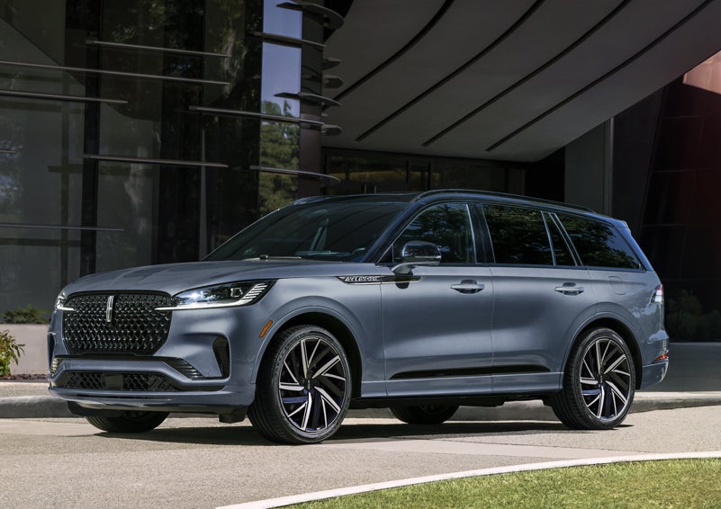 A gray 2025 Lincoln Aviator® SUV is parked outside a modern building showcasing the driver’s side of the vehicle. | Bill Collins Lincoln of Louisville in Louisville KY