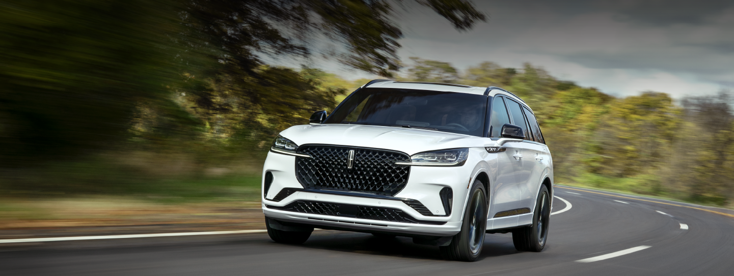 A white 2025 Lincoln Aviator® SUV is being driven down a road lined with trees. | Bill Collins Lincoln of Louisville in Louisville KY