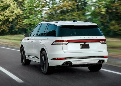 A white 2026 Lincoln Aviator® SUV is being driven away down a road lined with colorful trees. | Bill Collins Lincoln of Louisville in Louisville KY