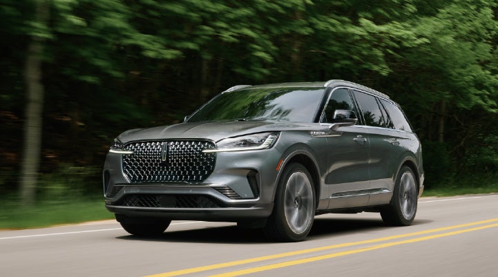 A 2027 Lincoln Aviator® SUV is being driven down a road lined with trees. | Bill Collins Lincoln of Louisville in Louisville KY
