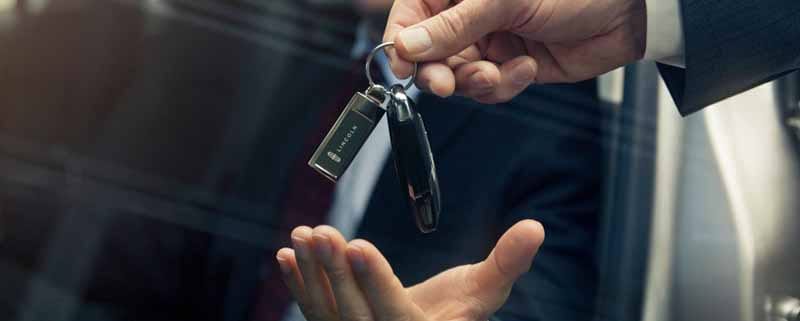 A smiling man sitting in a car being handed the keys