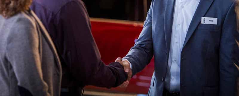 A car dealer shaking the hand of a man standing with a woman
